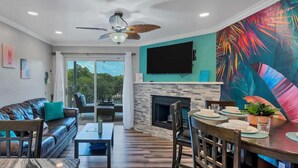 A modern living room with a fireplace, a dining area, and a balcony with a view. - River Front Condo: Close to Downtown and Gruene! (New Braunfels)