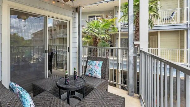 A balcony with wicker furniture and a glass door leading to a pool area. - River Front Condo: Close to Downtown and Gruene! (New Braunfels)