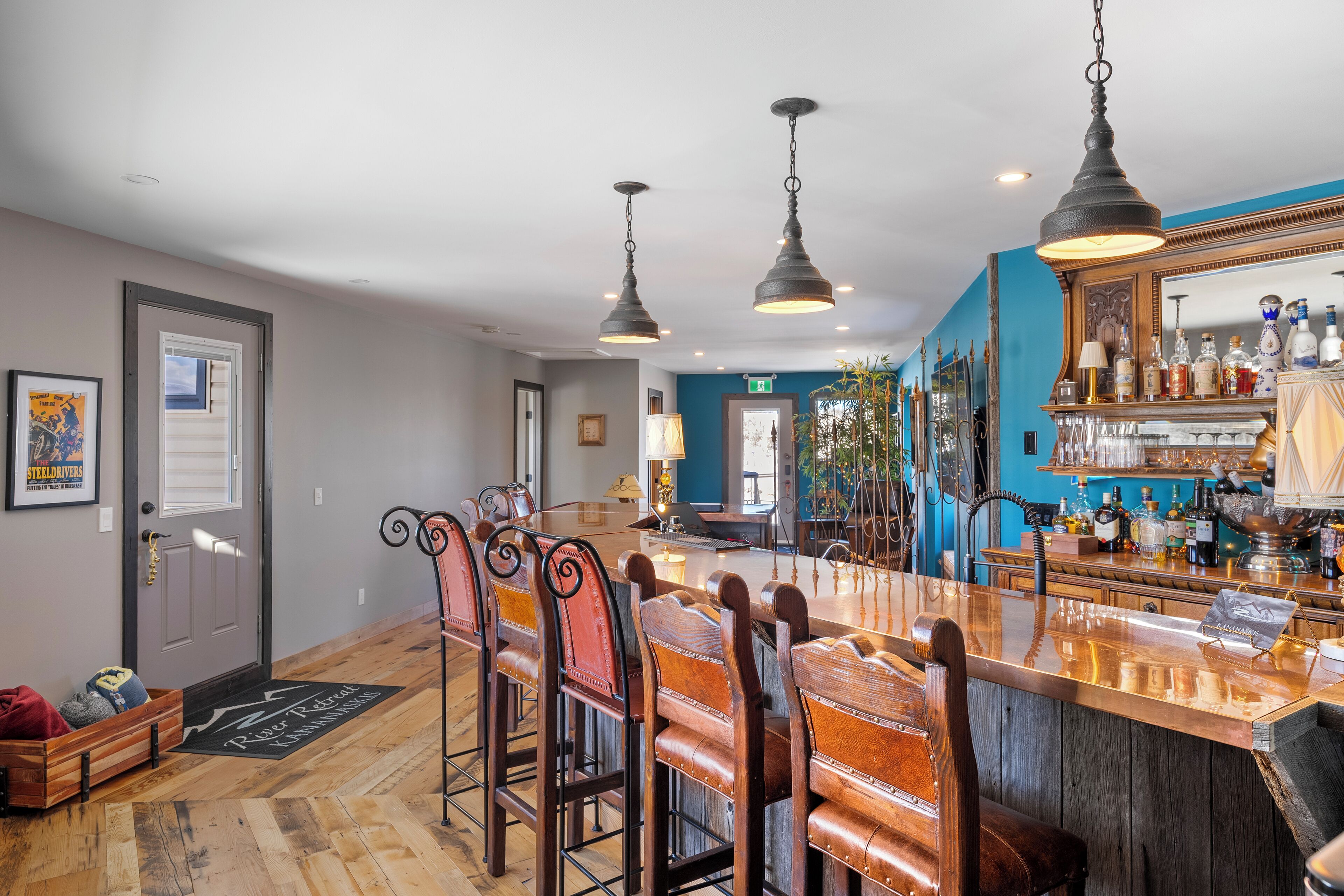 A bar area with a long counter, multiple bar stools, and hanging pendant lights.