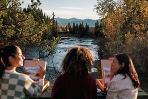 Trois personnes peignent en plein air, avec une rivière et des montagnes en arrière-plan.