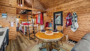 A wooden cabin interior with a round dining table, a loft bedroom, and a cozy living area. - River Retreat Kananaskis (Longview)