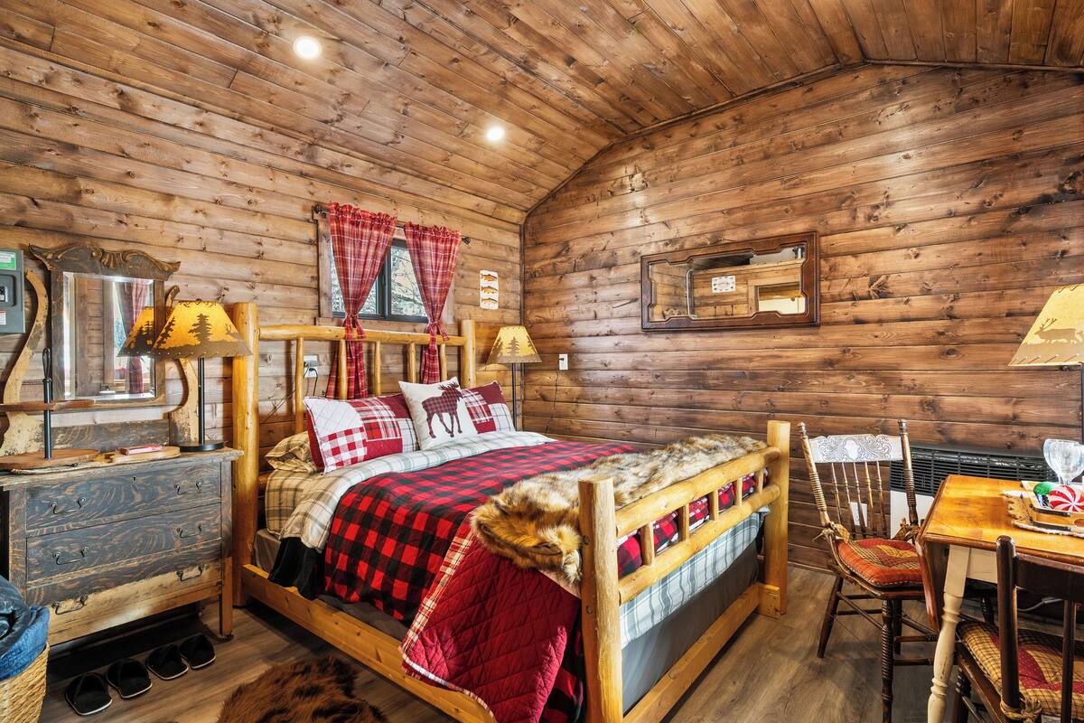 Habitació d'una cabana de fusta amb un llit, un taulell, una taula i una cadira.