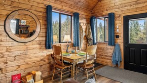 A wooden cabin interior with a dining table, chairs, a mirror, and a black door. - River Retreat Kananaskis (Longview)