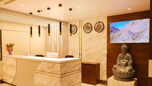 A reception area with a marble counter, a Buddha statue, wall clocks, and a TV displaying a mountainous landscape. - River sidde inn (Golmuri)