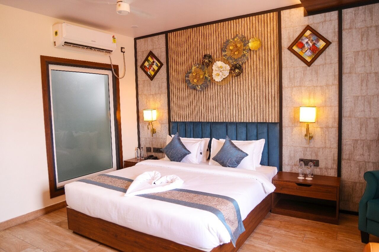 Habitación de hotel con una cama grande, cabecera de madera, dos lámparas fijadas a la pared y un panel decorativo.