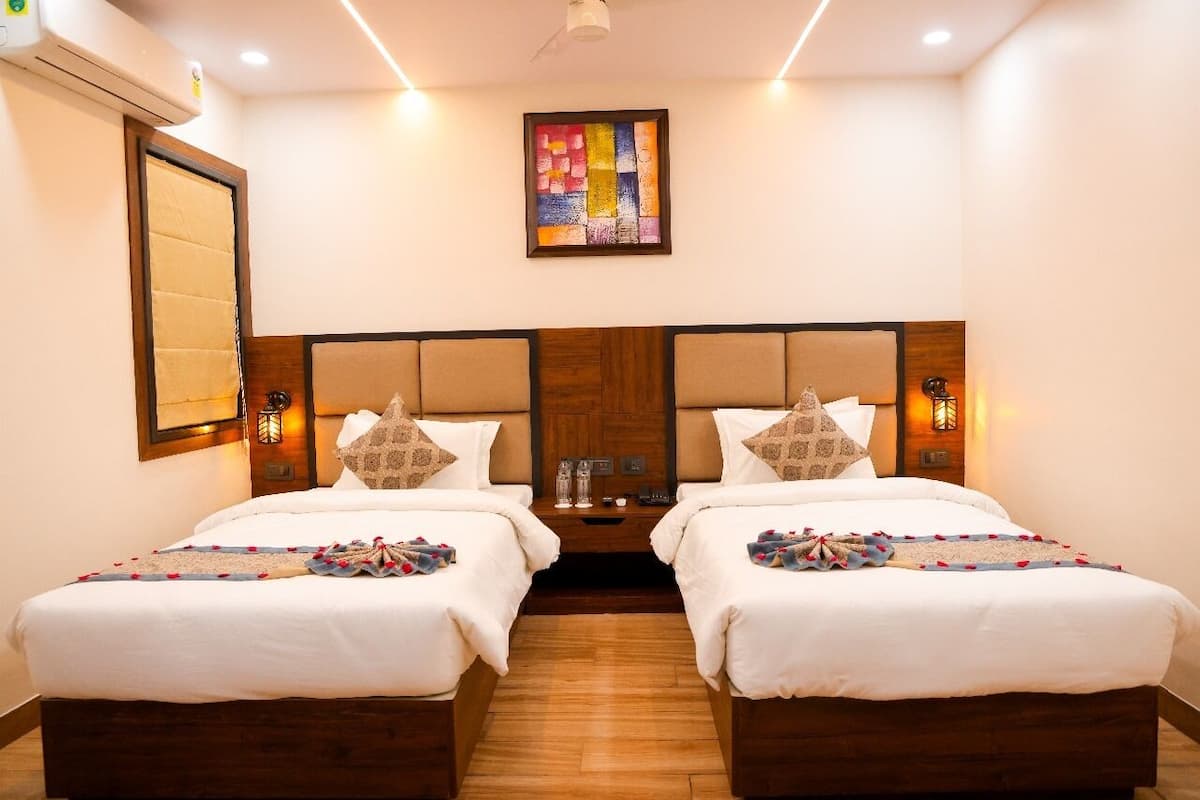 A hotel room with two single beds, a wooden headboard, a nightstand with a lamp, and a framed artwork on the wall.