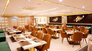 A modern restaurant with long tables, green cushioned seating, and a decorative wall with circular patterns. - River sidde inn (Golmuri)