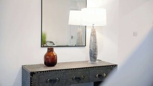 Un miroir au design simple et moderne, un vase et une lampe posés sur une commode à la texture intéressante.