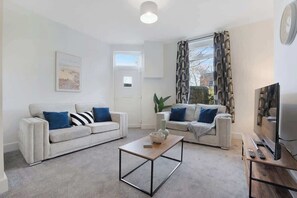 A modern living room with two sofas, a coffee table, a TV, and a window with curtains.