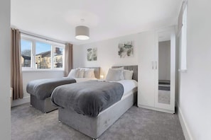 A bedroom with two beds, a window, and a door leading to another room.