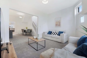 A modern living room with a sofa, coffee table, and a staircase leading to an open kitchen area.