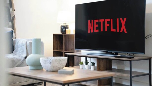 Un salon moderne doté d’un grand téléviseur à écran plat affichant le logo « NETFLIX », d’un canapé, d’une table basse agrémentée d’objets décoratifs et d’une petite table d’appoint avec une lampe.
