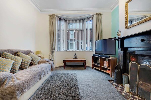 A living room with a sofa, television, fireplace, and a window with curtains.