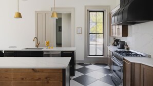 Cocina moderna con una isla grande, suelo a cuadros blancos y negros, electrodomésticos de acero inoxidable e iluminación colgante.