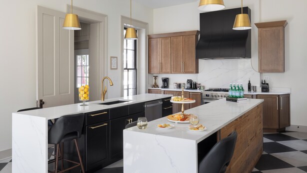 Una cocina moderna con una isla central, muebles de cocina en blanco y negro, y lámparas colgantes doradas.