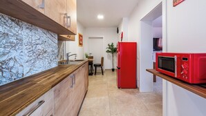 A modern kitchen with a marble countertop, wooden cabinets, a red refrigerator, and a microwave on a wooden shelf. - YS Apartments e.U. (Marchtrenk)