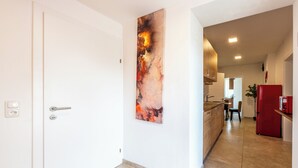 A hallway with a white door, a red refrigerator, and a kitchen area in the background. - YS Apartments e.U. (Marchtrenk)