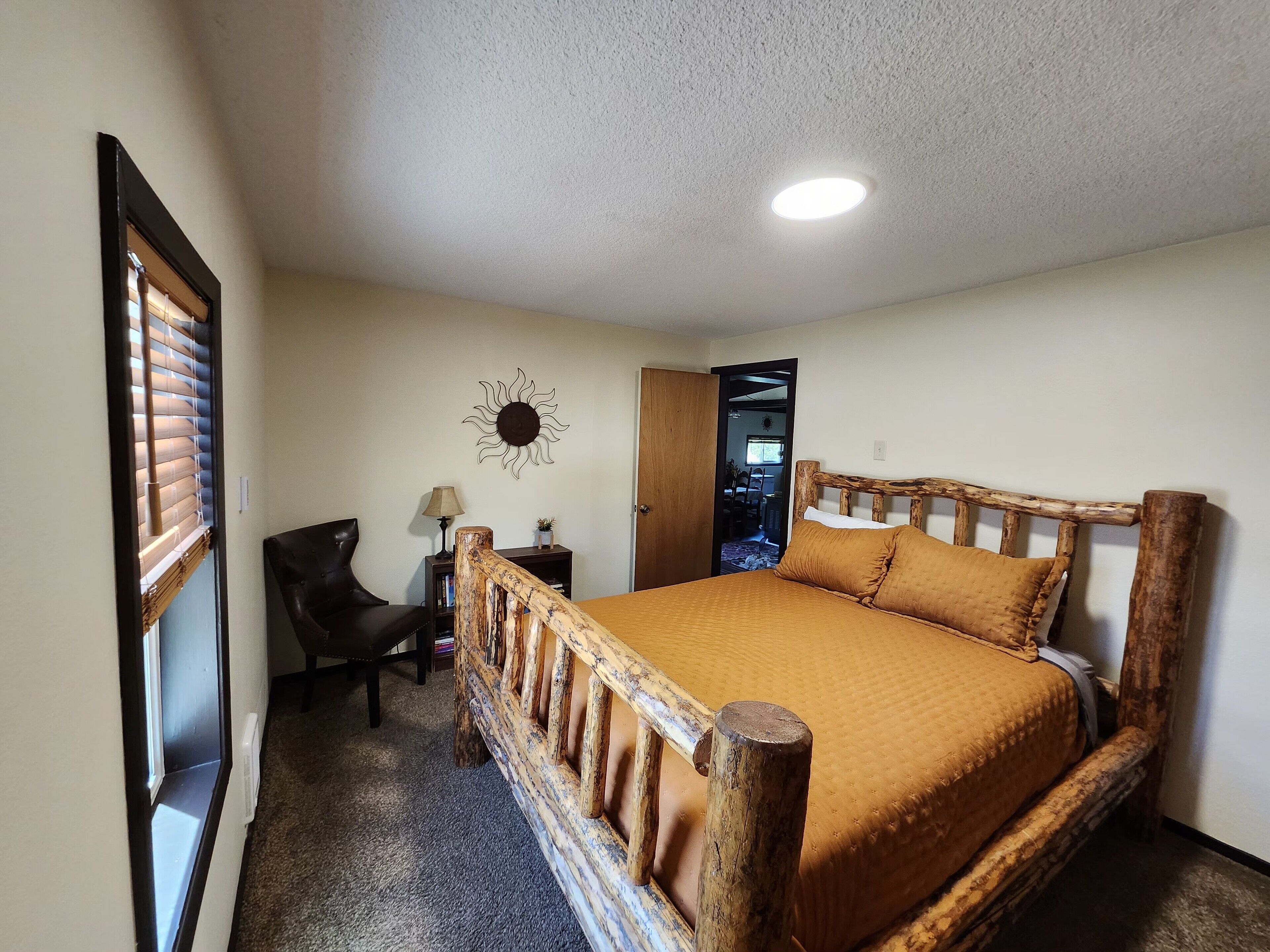 Un dormitorio con una cama de madera, un escritorio, una silla y una decoración de sol en la pared.