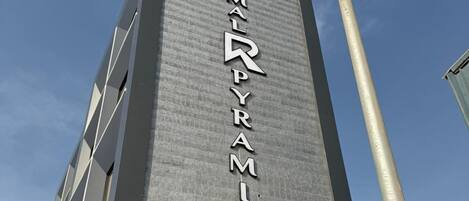 A tall hotel building with a modern design, featuring a prominent sign that reads "REYMALPYRAMIDS HOTEL".