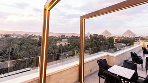 Una terraza en la azotea con vistas a las pirámides, palmeras y una vía de tren.