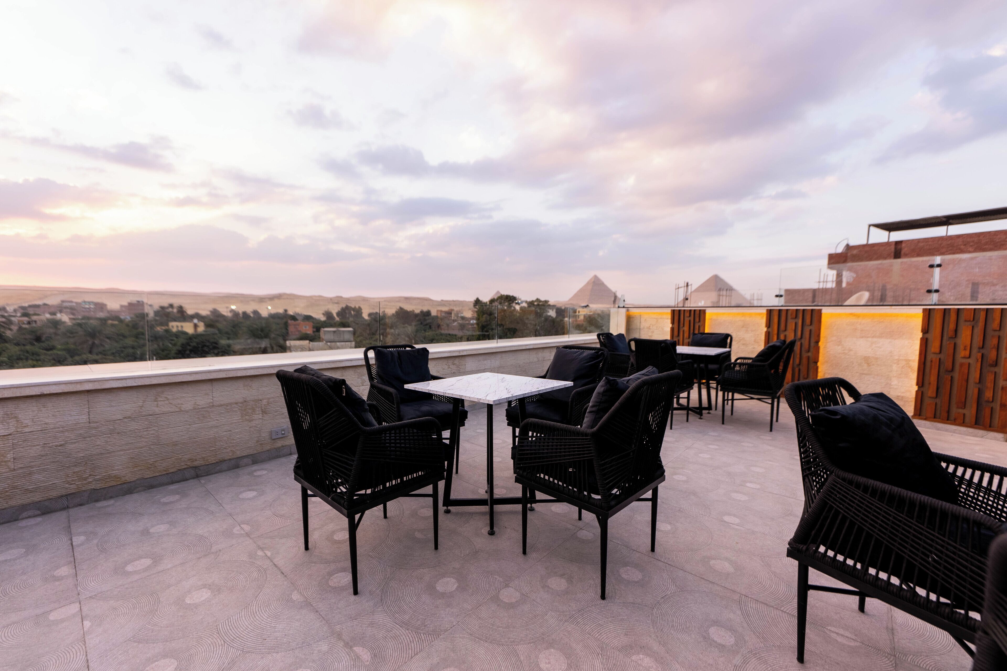 A rooftop terrace with wicker furniture and a view of pyramids.