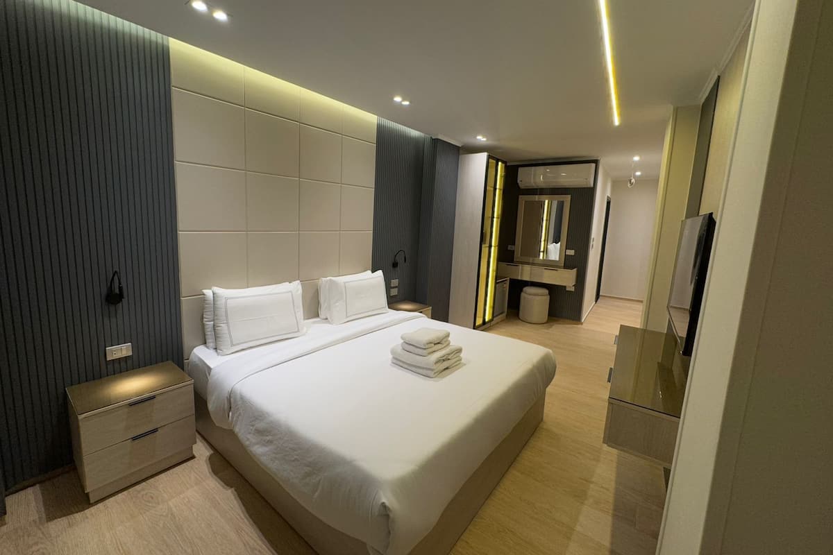 Une chambre d’hôtel moderne avec un grand lit, des tables de chevet, une coiffeuse avec un miroir et un téléviseur.