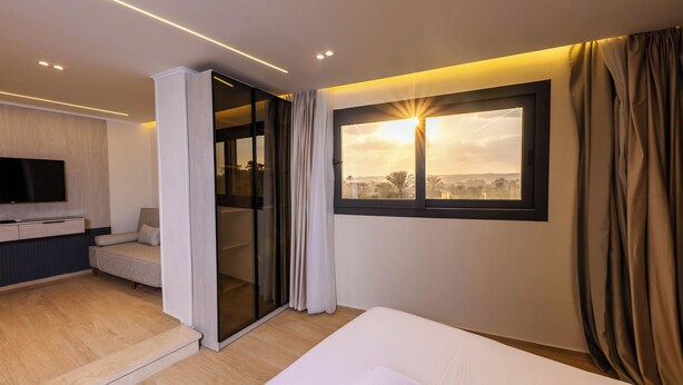 Una habitación de hotel moderna con cama, televisión, zona de estar y puerta corredera que da a un balcón.