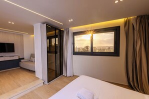 Una habitación de hotel moderna con cama, televisión, zona de estar y puerta corredera que da a un balcón.