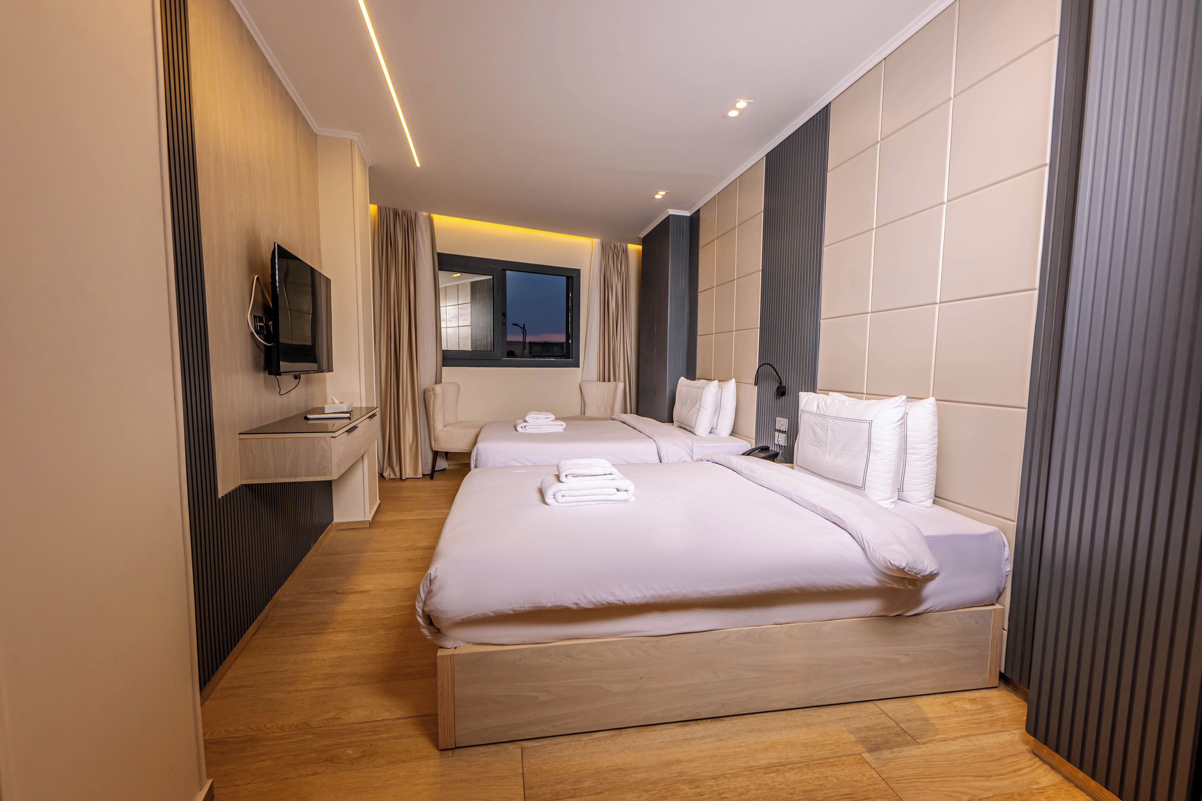 A modern hotel room with a large bed, a TV mounted on the wall, and a window with curtains.