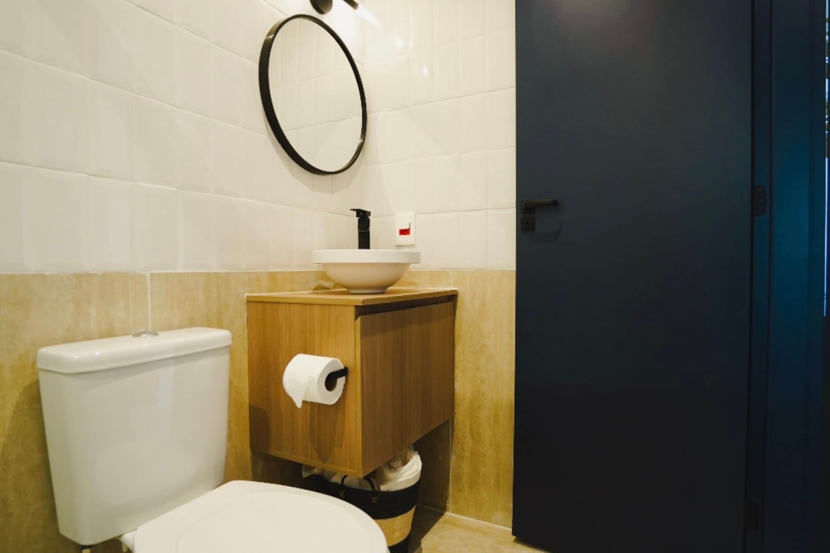 A bathroom with a toilet, a sink with a wooden cabinet, a toilet paper roll, and a dark door.