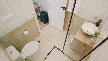 Un baño moderno con cabina de ducha de vidrio, un lavabo blanco y un inodoro.