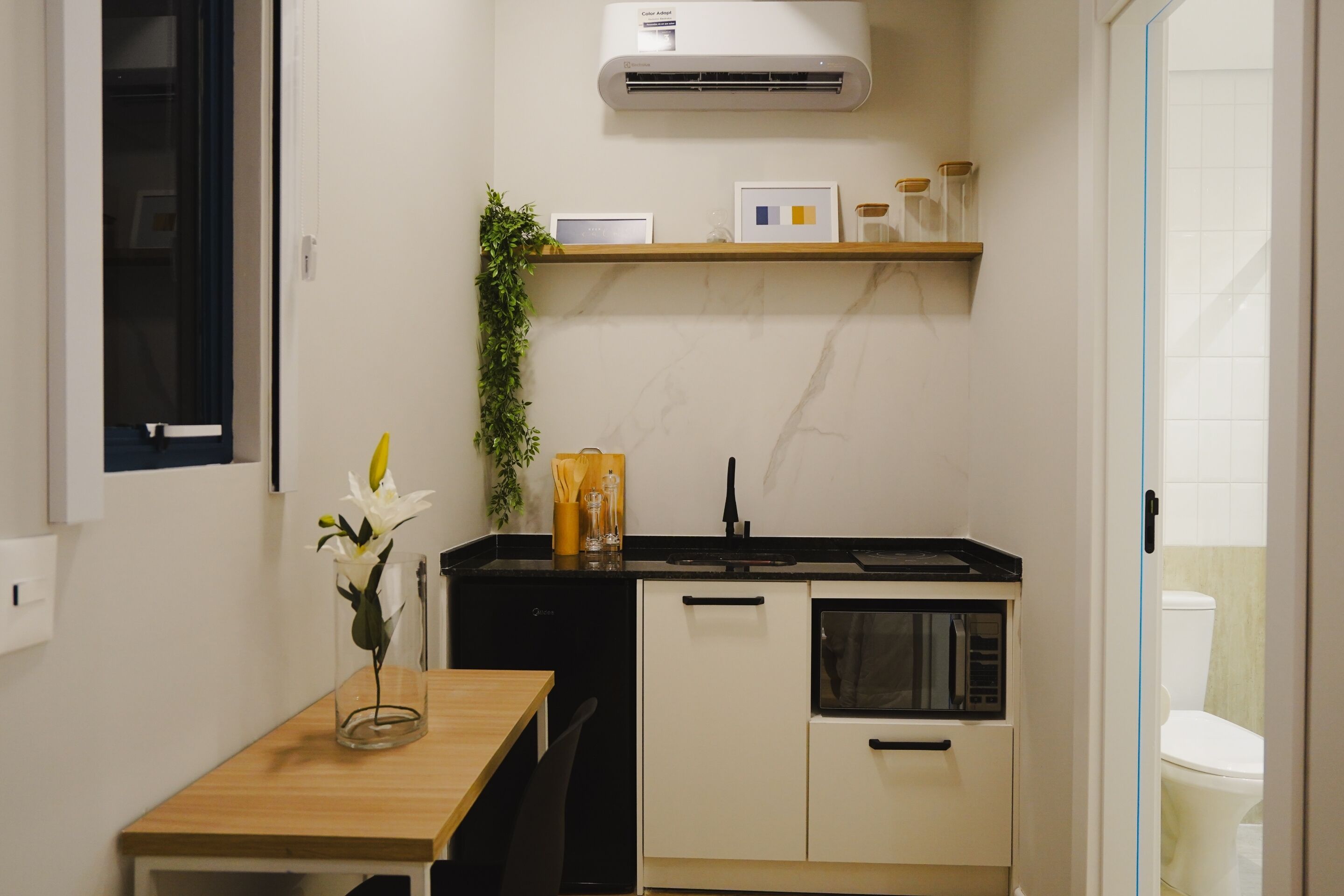 Una cocina compacta con una mesa de madera, un lavamanos negro y un refrigerador blanco.