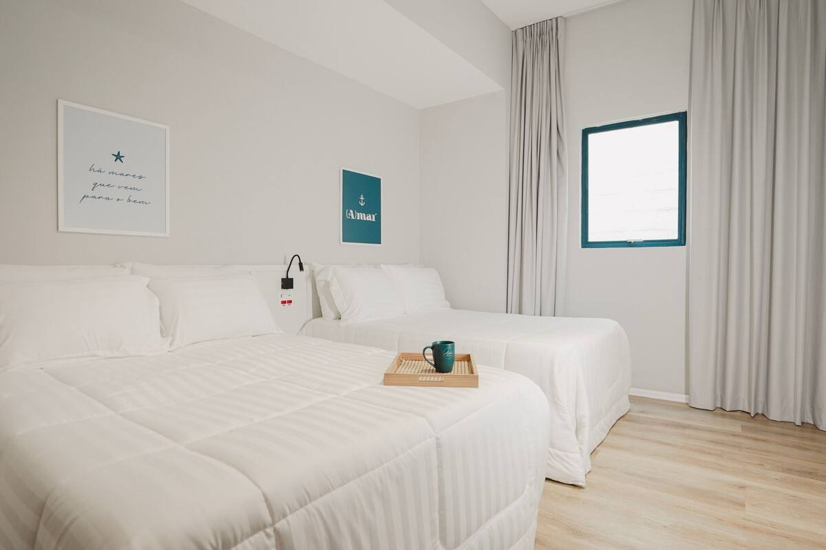 Ein Hotelzimmer mit zwei Betten, einem Fenster mit Vorhängen und einer Wand mit zwei gerahmten Bildern.