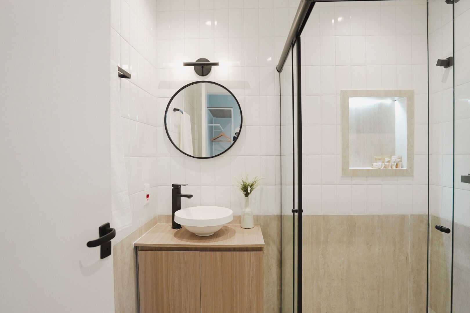 Ein modernes Badezimmer mit rundem Spiegel, Waschbecken in Weiß und einer Duschkabine aus Glas.