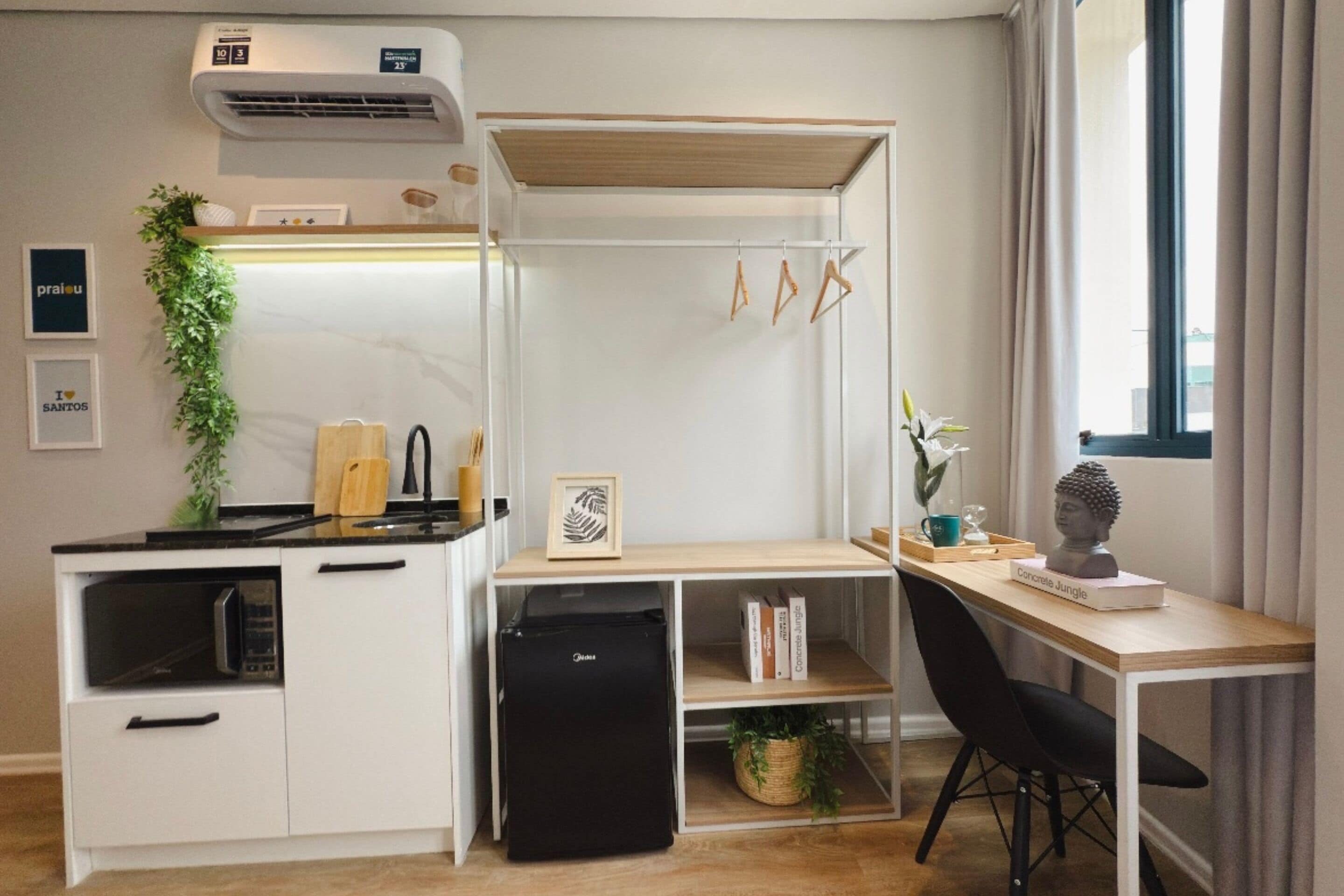 Une petite cuisine équipée d’un micro-ondes, d’un réfrigérateur et d’un petit évier. On y trouve un bureau en bois avec une chaise, une petite étagère avec des livres et une plante en pot.