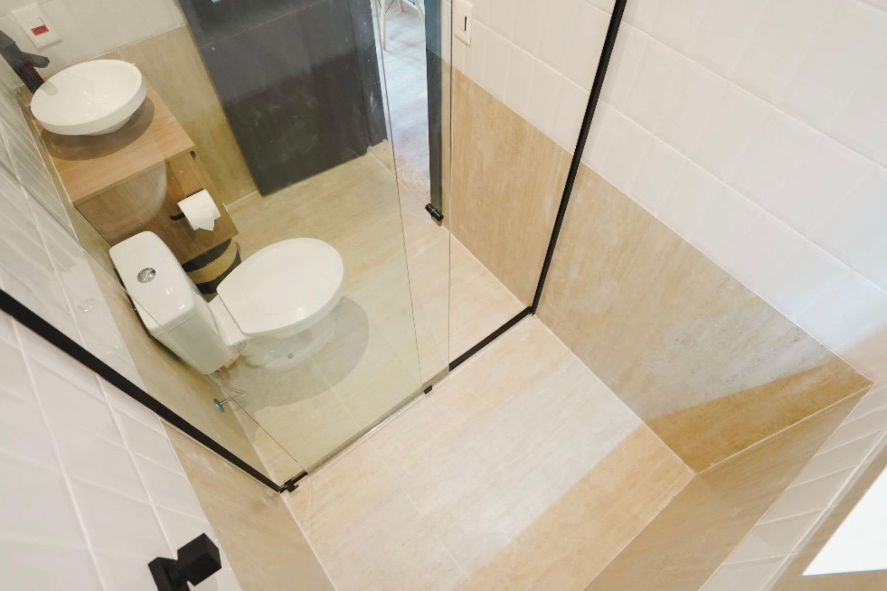 A modern bathroom with a glass shower enclosure, two toilets, and a sink.