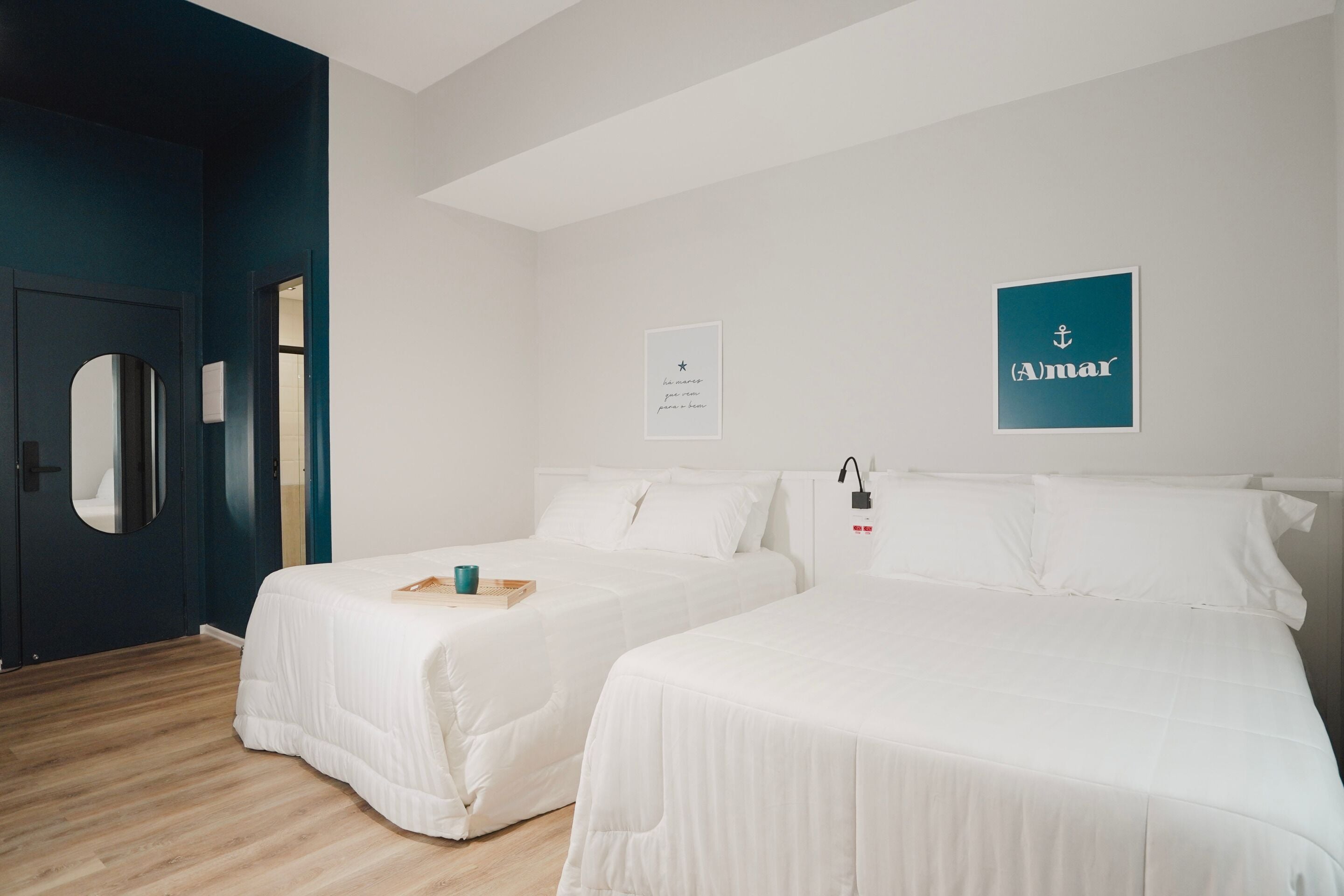 Une chambre d’hôtel avec deux lits, un miroir, une porte et un mur orné d’un tableau encadré et d’une enseigne.