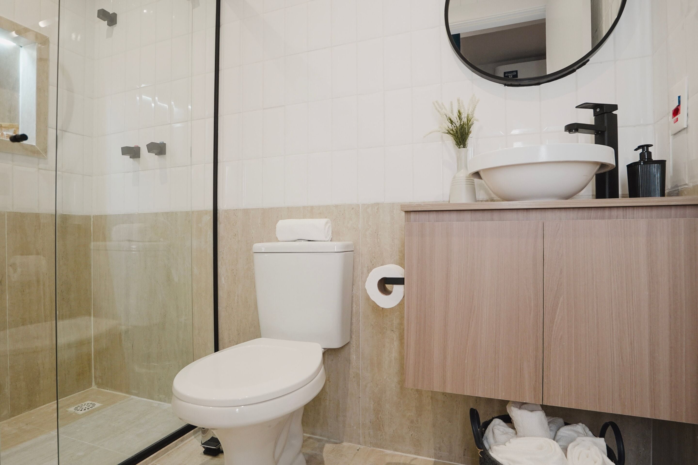 Une salle de bain moderne avec une douche à parois de verre, des toilettes, un lavabo avec un miroir et un meuble contenant des serviettes.