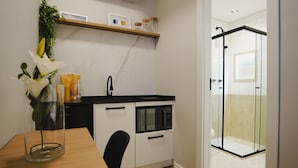 Eine kompakte Küche mit Mikrowelle, Spüle und einer Duschkabine aus Glas.