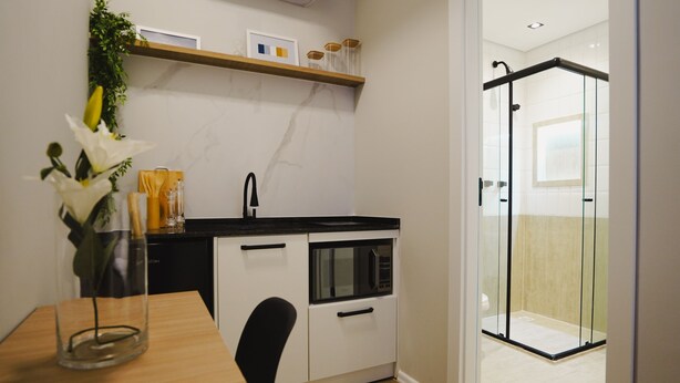 A compact kitchen with a microwave, a sink, and a glass shower enclosure. - Apê Santos Gonzaga (Santos)