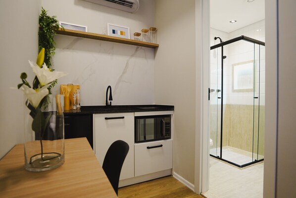 Cocina compacta con microondas, un lavamanos y cabina de ducha de vidrio.