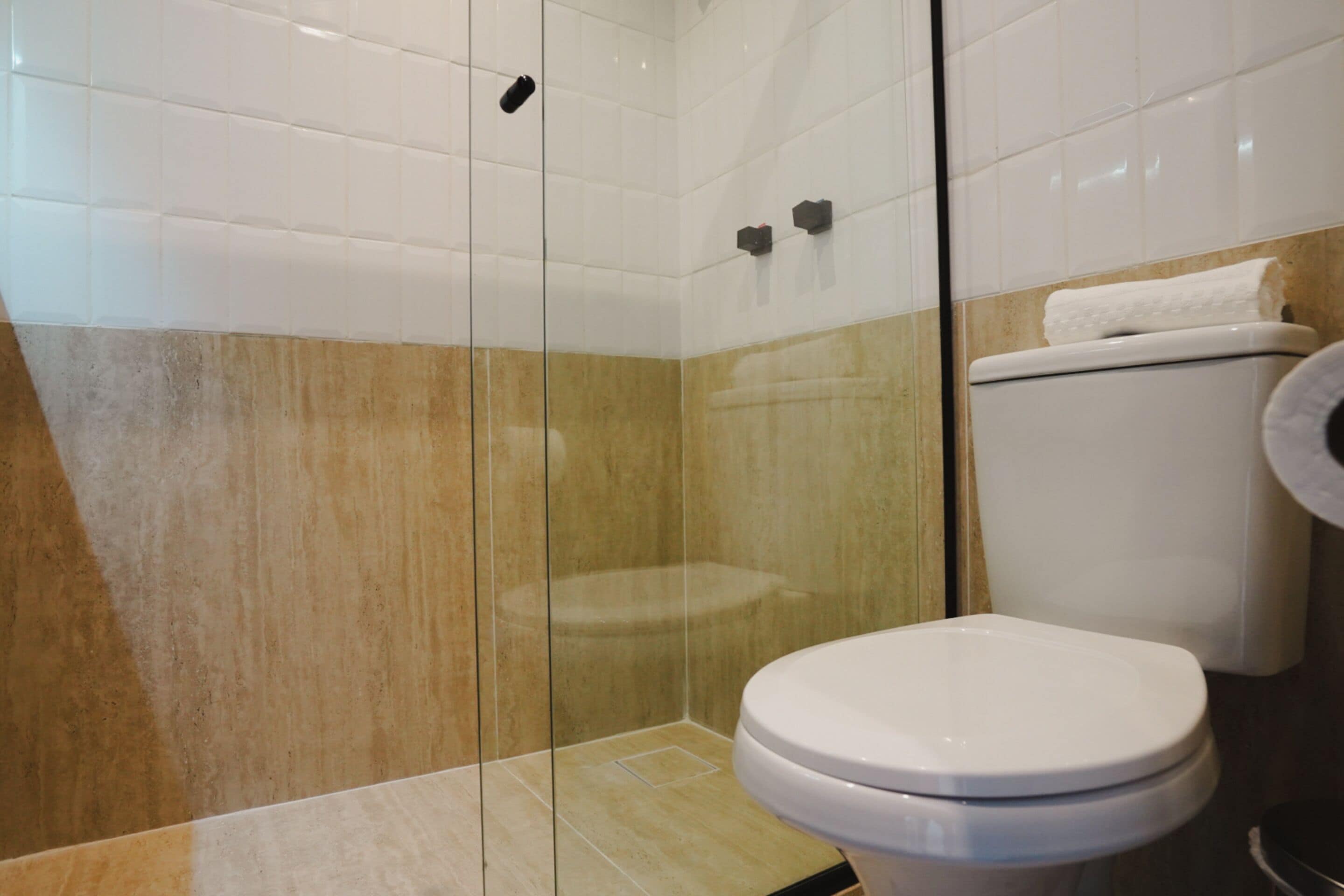 Ein Badezimmer mit Duschkabine aus Glas, einer weißen Toilette und einer beige gefliesten Wand.
