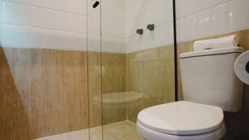 A bathroom with a glass shower enclosure, a white toilet, and a beige tiled wall.