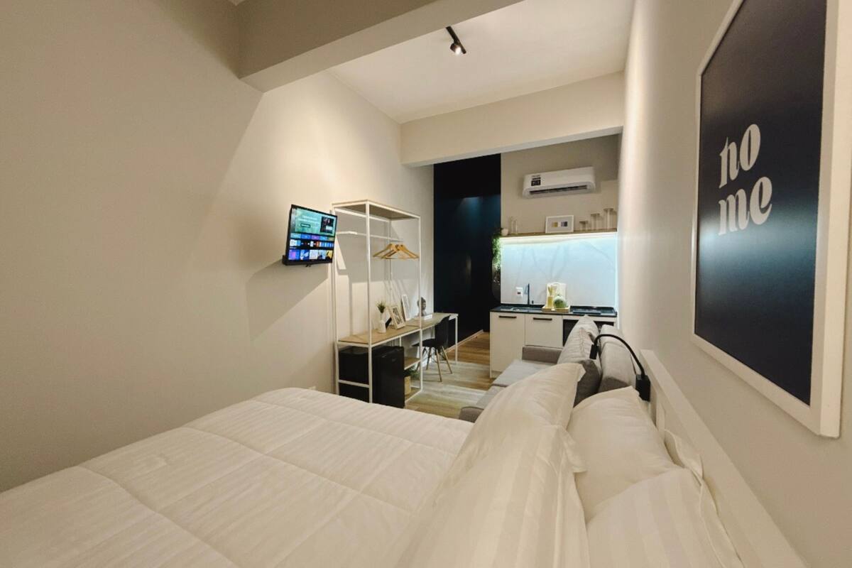 Ein modernes Schlafzimmer mit Bett, Schreibtisch und Stuhl. An der Wand ist ein Fernseher angebracht und ein Schild mit der Aufschrift 'home'.