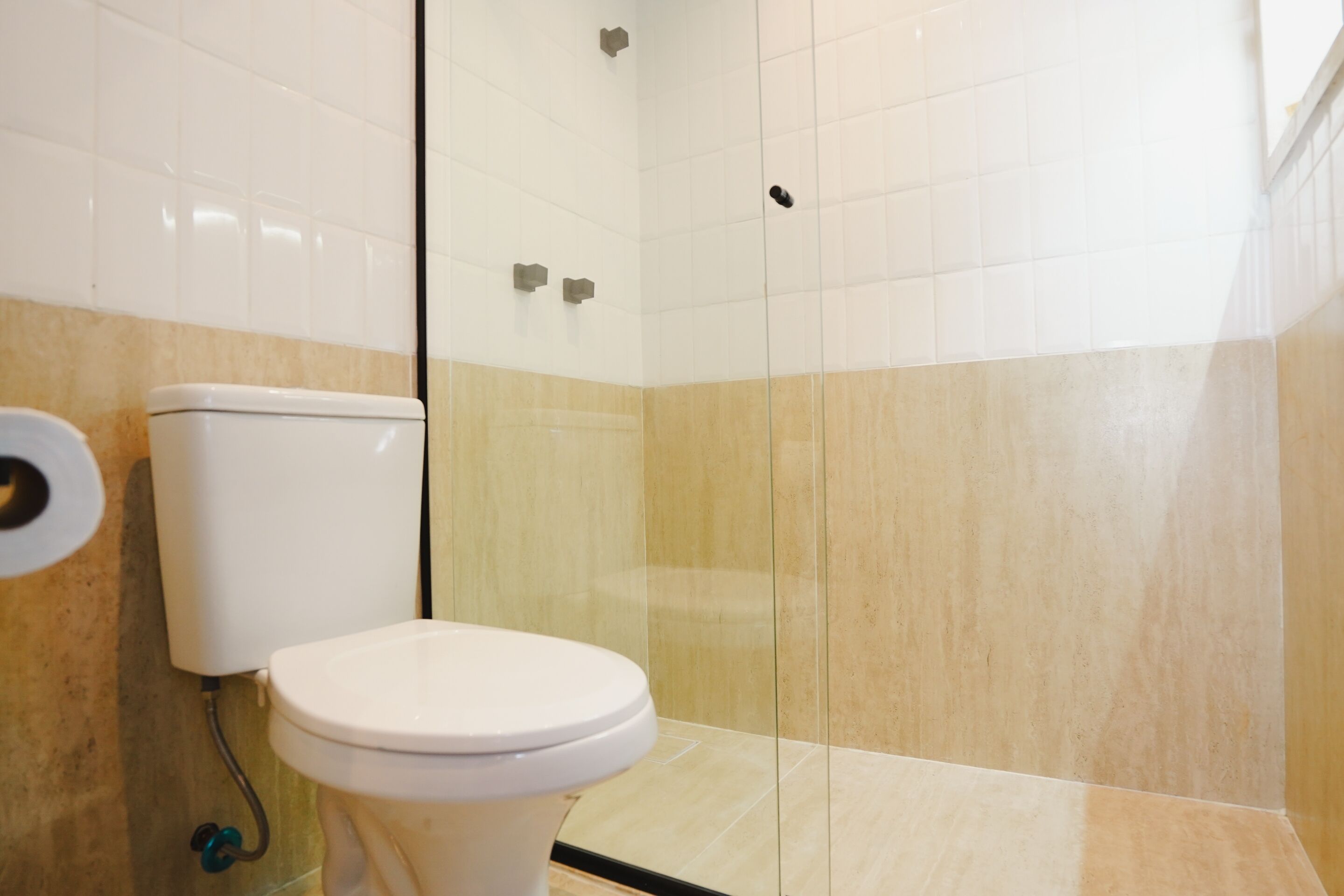 A bathroom with a toilet, a glass shower enclosure, and beige tiled walls.