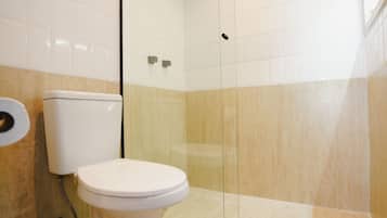 A bathroom with a toilet, a glass shower enclosure, and beige tiled walls.