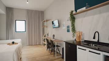 Una habitación de hotel moderna con una cama, un escritorio, un televisor, una zona de cocina y una ventana.