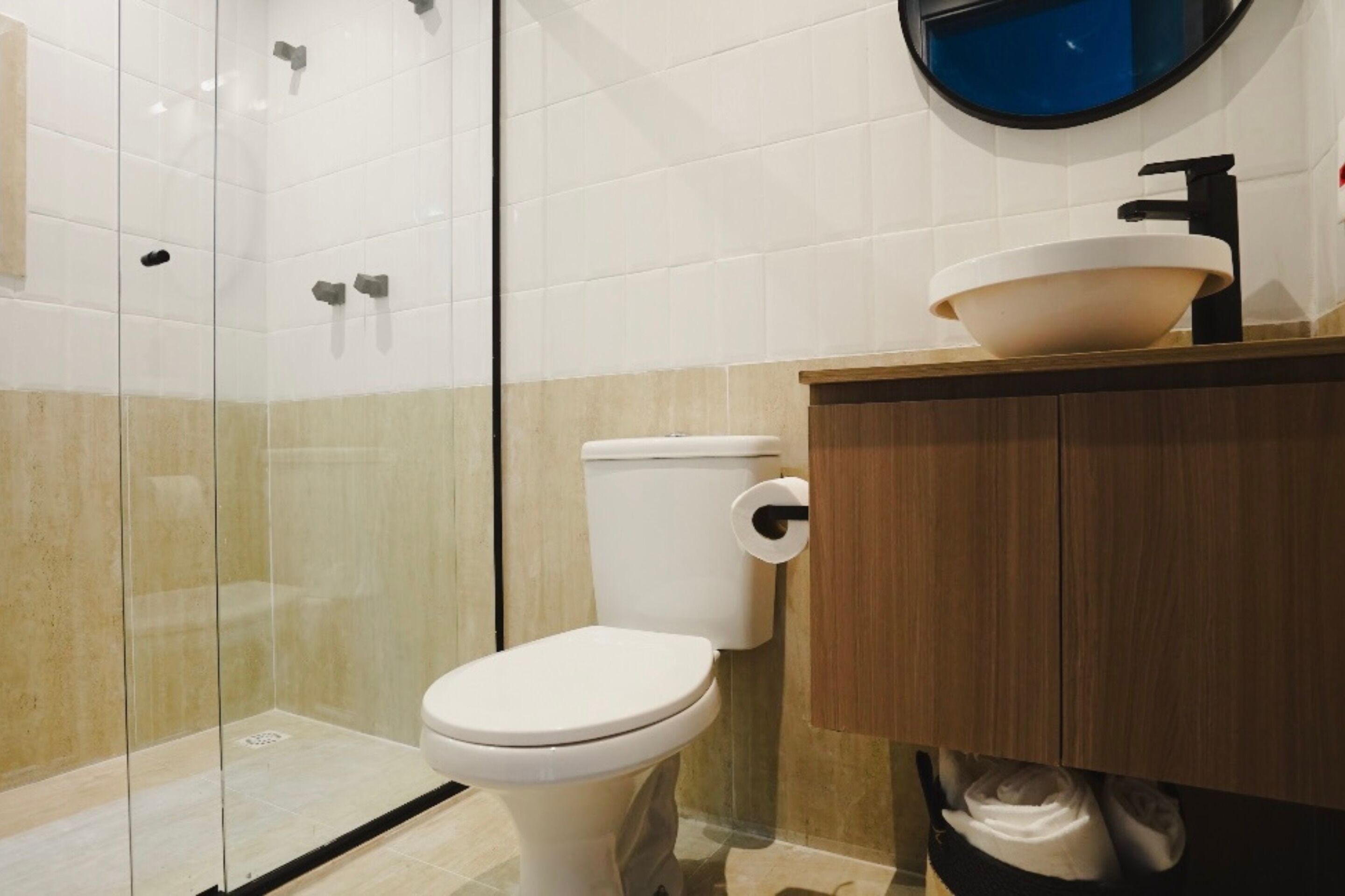 Un baño moderno con cabina de ducha de vidrio, inodoro blanco y tocador de madera con lavabo.