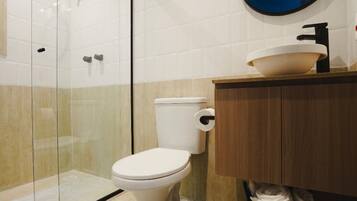 Un baño moderno con cabina de ducha de vidrio, inodoro blanco y tocador de madera con lavabo.