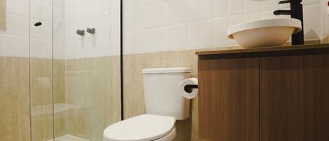 Ein modernes Badezimmer mit Duschkabine aus Glas, Toilette in Weiß und einem Holzkosmetikschrank mit Waschbecken.